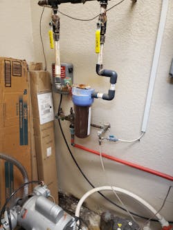 In utility room is a mercury/amalgam collector with blue top connected to a suction (vacuum) line. The collection unit is filled to overcapacity with mercury/amalgam waste (hazardous waste). There are fluid leaks at joints in plumbing, which contains human blood, saliva, mercury, and human tissue. Note biohazard precipitant buildup on pipes. See the biohazard leak onto floor and drywall particleboard destruction. This equipment at this stage should only be corrected by a licensed plumber or dental service specialist with full knowledge and certified training in PPE.
