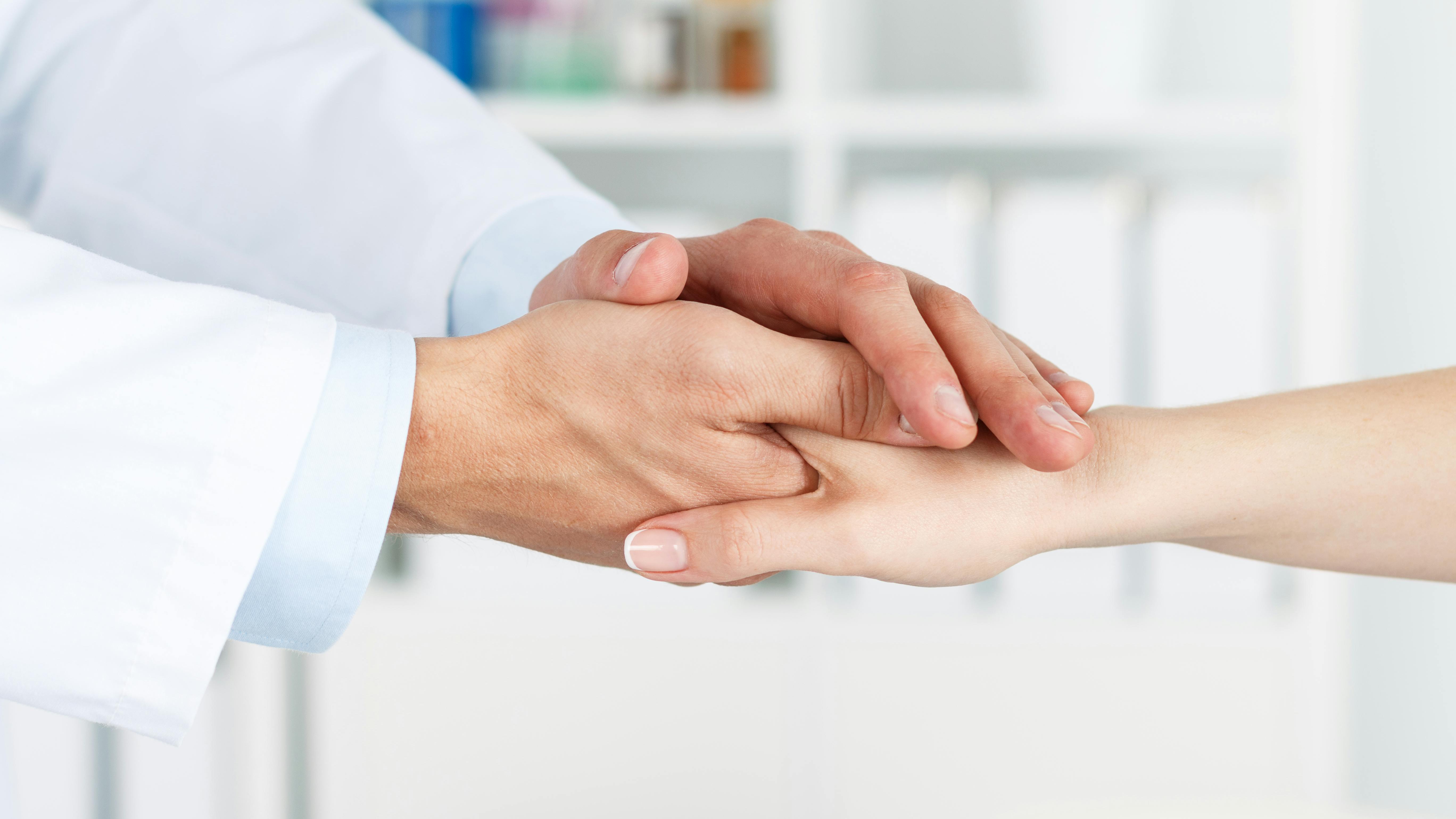 Friendly dentist's hands holding female patient's hand for encouragement and empathy.