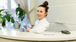 Dental office manager sits behind reception desk holding a file