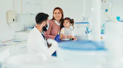 Dentist wearing face mask talking with mother and daughter during appointment in dental office, explaining treatment and giving advice for oral hygiene